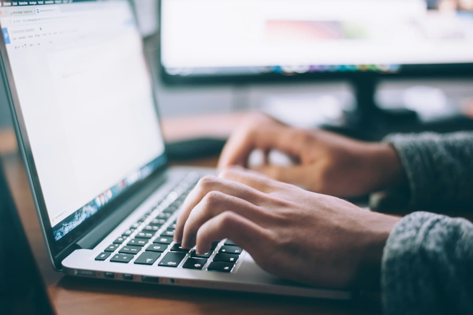 Hands typing on a laptop at a desk